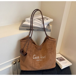 Detail showing the brown suede tote bag with white letter embroidery and leather charm