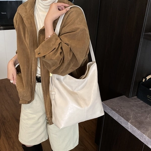 Détail du sac hobo en cuir blanc cassé avec boucle dorée sur veste en daim marron