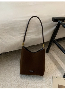 Detail of dark brown suede shoulder bag featuring minimalist design and gold hardware