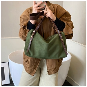 Detail of dark green suede tote bag showing brown leather strap and gold metal buckles