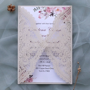 Close-up of laser cut lace wedding invitation with floral insert on soft tulle fabric