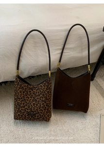 Detail of leopard print and dark brown suede underarm bags on a plush white carpet