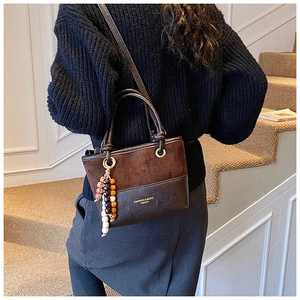 Close-up of brown suede tote bag with circular metal ring and wooden beaded tassel detail