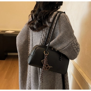Détail du sac à bandoulière en cuir grainé noir avec texte doré et pendentif décoratif