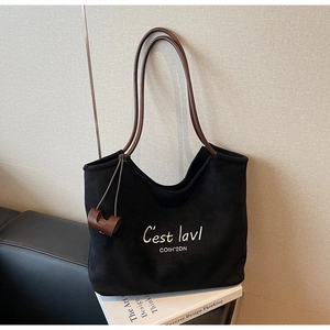 Detail of black suede tote bag with white embroidery and contrasting brown leather handle