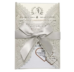 Detail of laser cut lace wedding invitation with silver satin bow and floral patterns