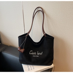 Detail of black suede tote bag featuring white letter embroidery and brown leather straps