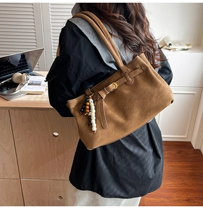 Brown suede bucket bag with beaded tassel charm shown on model in modern office
