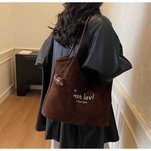 Detail of a brown suede tote bag featuring white letter embroidery and a round leather charm