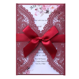 Detail of laser-cut burgundy wedding invitation with red silk ribbon and white floral insert