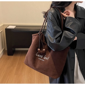 Detail of dark brown suede tote bag with white embroidery and saddle shaped pendant