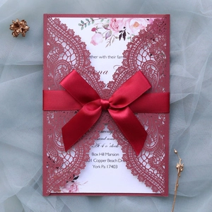 Detail of red laser cut wedding invitation with lace pattern and silk ribbon bow