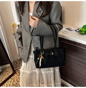 Close-up of black matte suede bucket bag with vintage leather strap and beaded charm