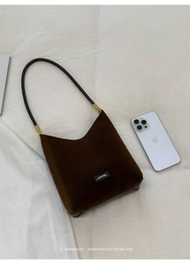 Detailed top view of dark coffee suede shoulder bag on white fabric with phone for scale