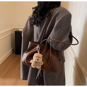 Détail d'un grand sac cabas en daim marron foncé avec pendentif chien sur l'épaule