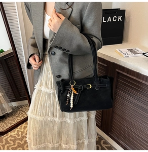 Detail of black suede bucket bag featuring decorative gold buckle and beaded fringe tassel