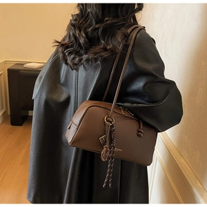 Détail du sac bowling en cuir marron grainé avec pompon et breloques métalliques chic