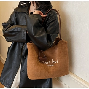 Detailed view of large brown suede tote bag with white cursive embroidery on black jacket