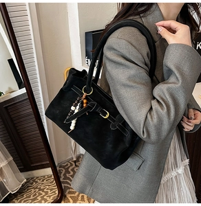 Detail of black suede bucket bag featuring chic beaded tassels and buckled strap detail