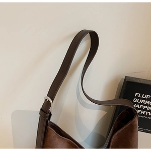 Detail of adjustable leather strap and silver metal buckle on a brown suede bucket bag