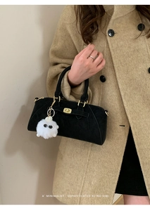 Dettaglio borsa in camoscio nero con chiusura dorata e ciondolo su cappotto kaki