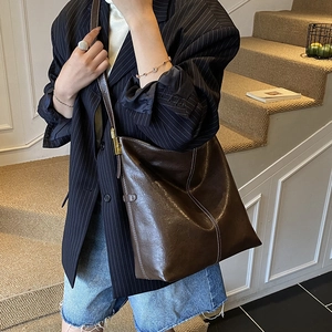 Détail d'un grand sac bandoulière marron foncé avec surpiqûres et boucle métallique dorée