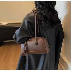 Detail of vintage brown litchi leather bowling bag with gold logo on a model shoulder