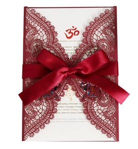 Macro detail of laser-cut red lace wedding invitation with silk bow and printed insert