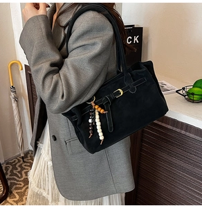 Detail of black suede bucket bag featuring vintage buckle and colorful beaded tassel charm