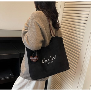 Detail of black canvas tote bag with white embroidery and brown leather straps on model