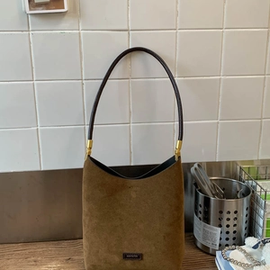 Close-up of brown suede shoulder bag with thin straps and NOFILTER logo on a metal table