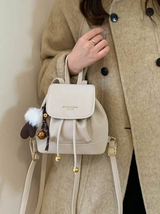 Chic beige drawstring backpack with gold hardware and plush heart charm on a model