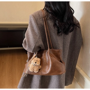 Détail d'un grand sac cabas en cuir marron foncé avec un pendentif ours en peluche doux