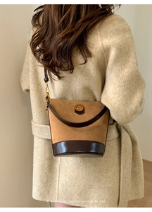 Detail view of brown suede bucket bag with leather base and gold logo on beige coat