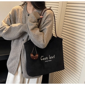 Detail of black matte tote bag with white embroidery and brown strap on a model