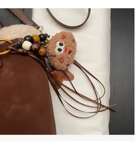 Détail du sac bandoulière marron en peluche avec breloque biscuit et pompon en bois