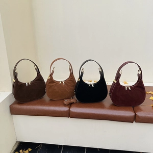 Detail of four suede hobo bags in autumn tones with gold hardware on a leather bench