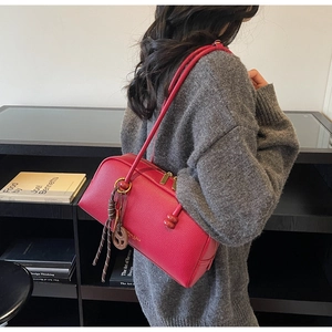 Sac bowling en cuir rouge à motif litchi porté à l'épaule par un mannequin en studio