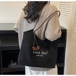Detail of black suede tote bag with white embroidery and brown leather strap