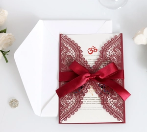 Detail of burgundy laser-cut wedding invitation with elegant lace pattern and satin ribbon bow