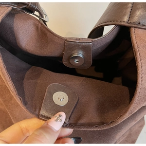Detail view of the silver magnetic buckle closure on a dark brown suede bucket bag