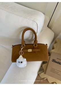 Dettaglio borsa a mano marrone con chiusura dorata e ciondolo di peluche bianco su divano