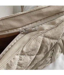 Detail shot of smooth metal zipper and diamond quilted texture on beige puffer tote bag