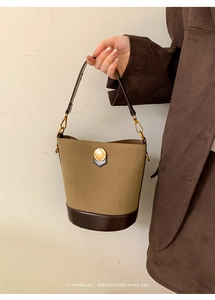 Detailed close-up of olive suede bucket bag with gold fashion emblem and brown leather trim
