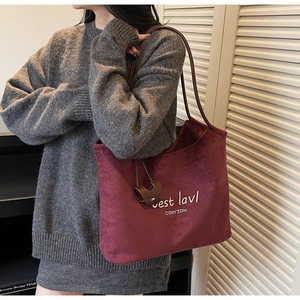 Detail of burgundy suede tote bag featuring white artistic lettering and leather straps