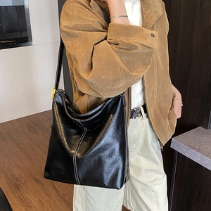 Détail du sac seau en cuir verni noir avec surpiqûres blanches et large bandoulière