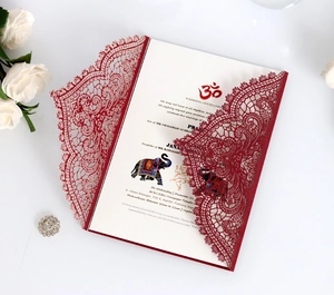 Detail of laser cut wedding invitation with red lace pattern and ornate Indian motifs