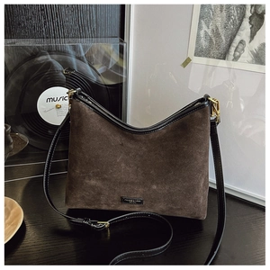 Dettaglio della borsa tote in pelle scamosciata marrone scuro con logo dorato e finiture in nero