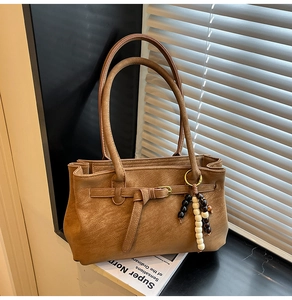 Detail of caramel brown tote bag with vintage leather texture and beaded ornament charm