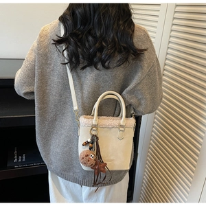 Detail of model wearing a beige suede bucket bag with faux fur trim and cute charms